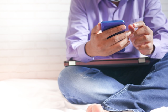 Eine Person sitzt auf einem Bett und benutzt ein Telefon.