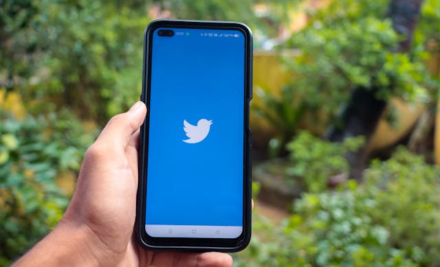 Someone holds a smartphone with the Twitter logo on the screen.