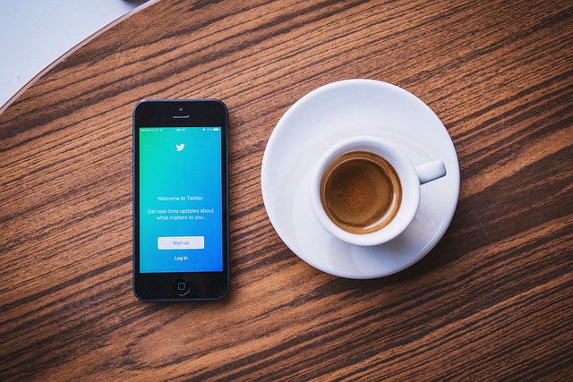 A mobile phone on a wooden table beside a cup of coffee displaying Twitter’s sign-up page.