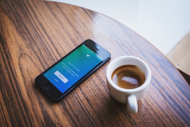 A phone with the Twitter login page on the screen beside a cup of coffee.